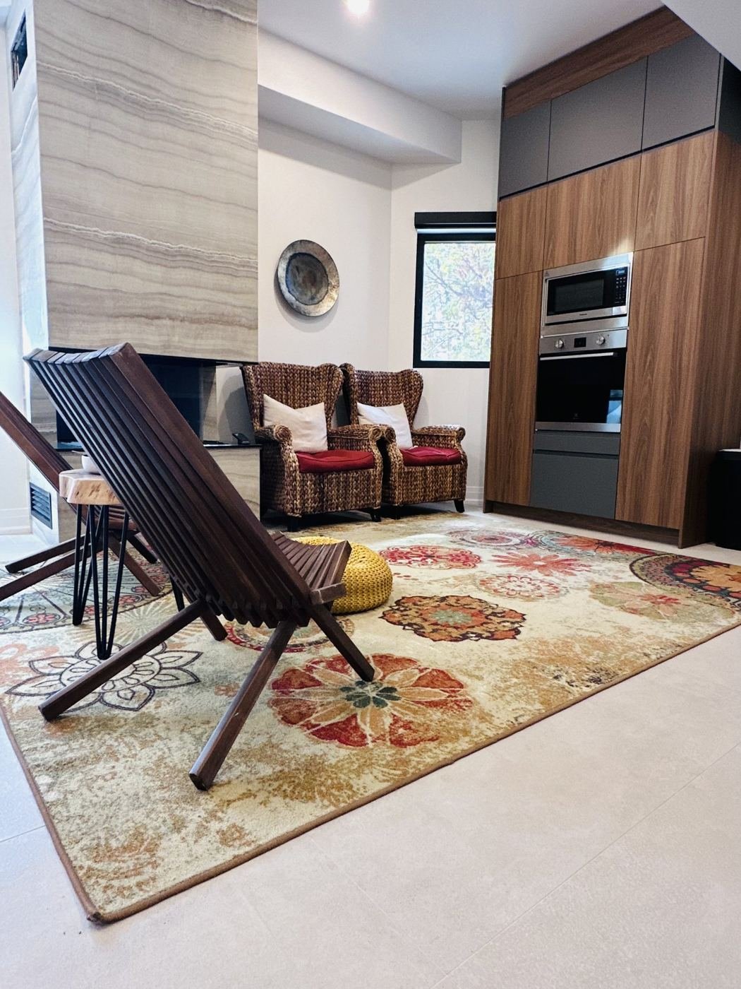Sitting area with slatted wooden lounge chairs, a patterned rug and a stone fireplace